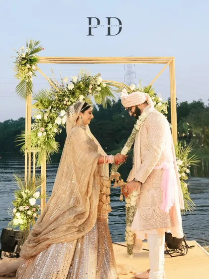 A beautiful varmala moment at a lakeside wedding. The minimal floral arch is designed to frame the couple perfectly without distracting from the natural beauty of the water behind them.