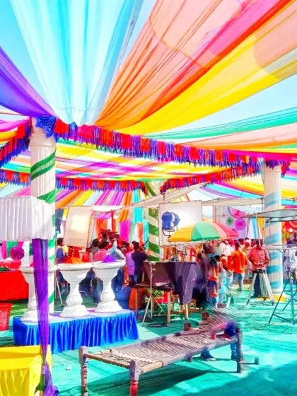 This is a large-scale Holi party pandal I decorated. I used vibrant, multi-colored fabric drapes across the ceiling and arranged traditional charpai seating to create a lively and authentic desi celebration space for the community.