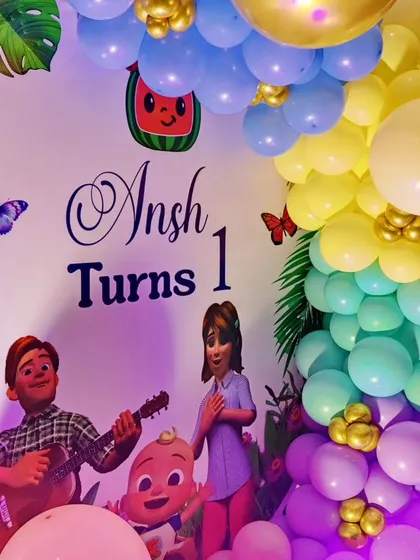 A joint Cocomelon and Boss Baby-themed first birthday. The backdrop features characters from both shows, surrounded by a rainbow balloon garland.