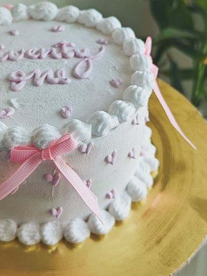 A side view of the "twenty one" cake, highlighting the soft pink ribbon and the scalloped buttercream border.