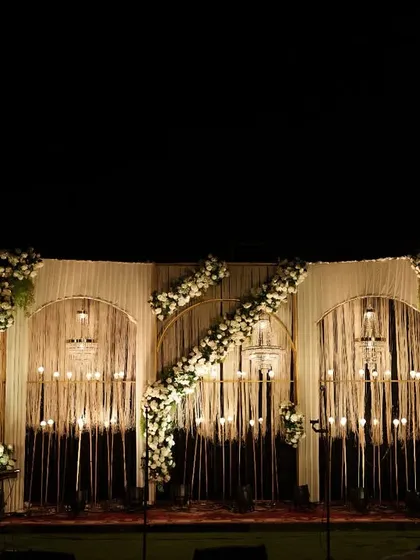We used warm lighting and cascading floral arrangements to create this romantic reception stage. The combination of delicate string lights and white flowers against a draped backdrop set a cozy and inviting mood.