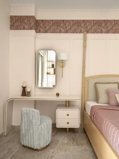 This master bedroom is all about soft luxury. A curved vanity table and a plush, fuzzy chair create a chic and feminine dressing corner. The wall features classic paneling with a decorative wallpaper border.