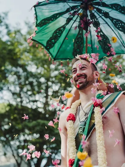 A groom from New Zealand joyfully participates in a South Indian wedding ritual, showered with flower petals.