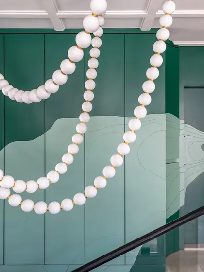 This dramatic staircase well is a focal point of the Evelyn duplex. The wall is treated as a single piece of art with a custom green facade that conceals storage, while the pearl necklace chandelier adds a touch of extravagant elegance.