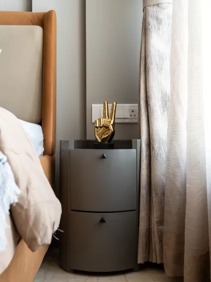 This elegantly curated bedroom corner exudes a harmonious blend of modern sophistication and understated luxury. The muted, earthy tones of the upholstered bed and sleek, curved bedside table create a seamless balance of warmth and contemporary minimalism.