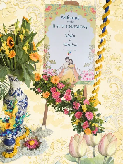 The personalized welcome easel for Nidhi and Manish's Haldi, beautifully decorated with fresh flowers.