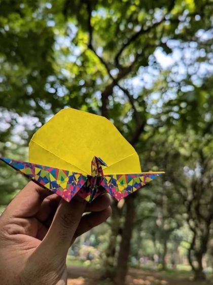 A beautiful origami crane held up against the backdrop of Cubbon Park's trees. We love collaborating with artists to bring activities like paper folding to our story circle.