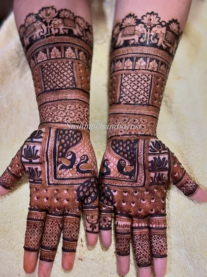 This design is filled with auspicious symbols. It features facing peacocks on the palms and a procession of elephants at the cuff, bringing a royal feel to the bridal mehandi.