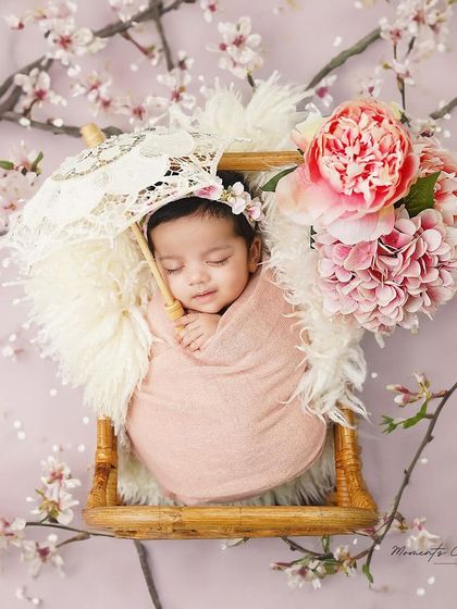 A dreamy floral escape. This newborn girl, swaddled in soft pink, sleeps peacefully in a basket surrounded by cherry blossoms and peonies.