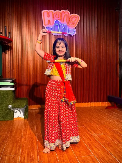 A joyful student in a traditional red and yellow Garba outfit. We encourage every child to express themselves through dance, and her happy expression says it all.