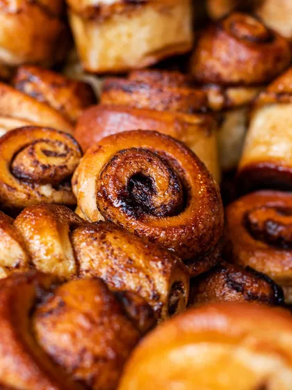 A tight close-up on sticky cinnamon rolls. The detail in the swirls and glistening glaze is designed to make them irresistible on a menu.