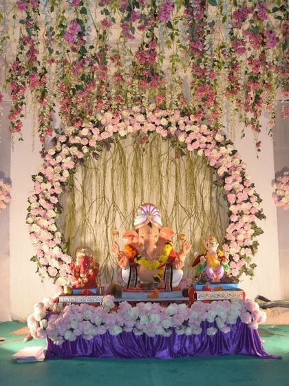 This large-scale decoration features a beautiful circular arch and a ceiling adorned with hanging pink flowers. It’s a design that fills the space with elegance and is perfect for larger idols and society pandals.