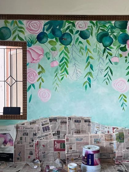 A work-in-progress shot of a hanging floral mural with a watercolor effect. The soft, blended colors and delicate flowers create a dreamy and romantic atmosphere behind a headboard.