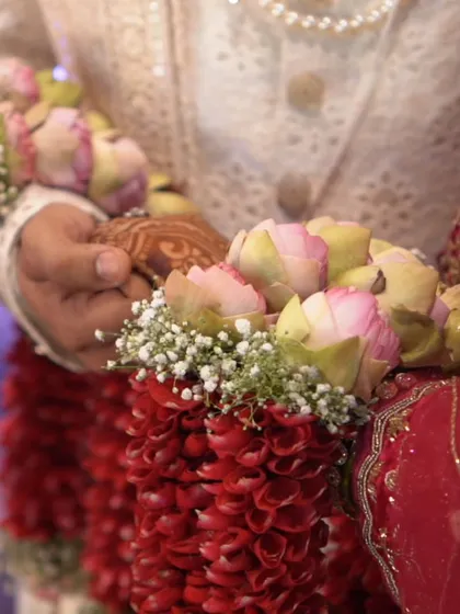 A close-up of the varmala exchange, focusing on the beautiful lotus garlands. This detail shot adds texture and richness to the wedding story.