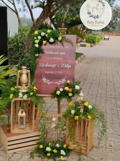 This rustic welcome setup uses wooden crates, vintage lanterns, and birdcages filled with flowers. The personalized wooden sign warmly greets guests, creating a charming and personalized entryway for the wedding.