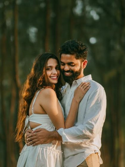 A beautiful, sun-dappled portrait of the couple in the woods. The golden light filtering through the trees creates a magical, romantic effect.