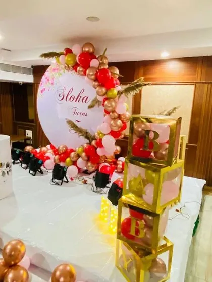 A floral-themed 5th birthday decoration with a red and rose gold balloon arch and custom-printed plinths.