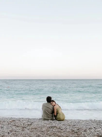 A serene scene on a pebble beach in Nice. This portrait of the couple looking out at the sea captures a feeling of peaceful love and shared dreams.