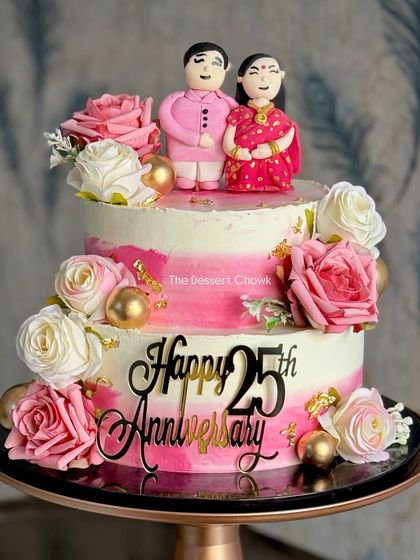 Celebrating 25 years of love with this stunning two-tier anniversary cake. It features a pink ombre design, fresh flowers, and adorable custom fondant toppers of the couple in traditional attire.