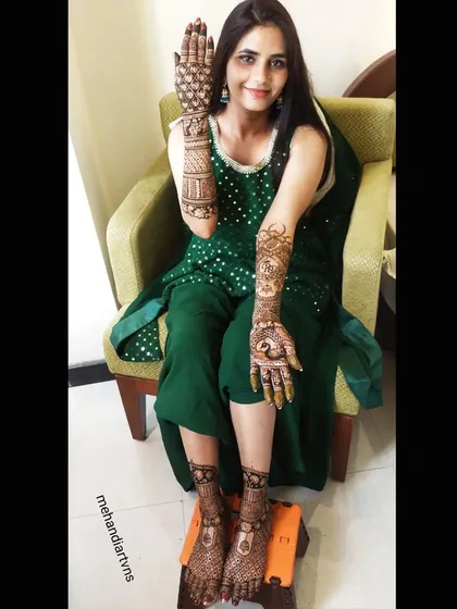 A happy bride displaying her full set of wedding mehandi. The designs on her hands and feet are beautifully matched for a harmonious look.
