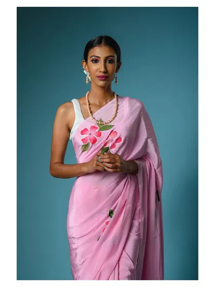 A beautiful studio portrait featuring a model in a hand-painted pink saree. The clean blue background makes the soft pink color stand out, perfect for a spring or summer collection.
