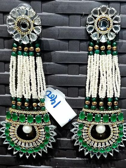 A very grand and long pair of earrings for a truly dramatic look. They feature a kundan top with long strings of pearls and a large green stone design at the bottom, perfect for a bridal ensemble.