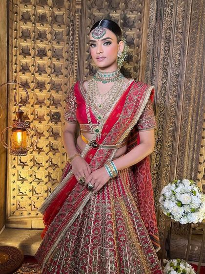A full-length view of the red and green bridal lehenga. The makeup, hair, and outfit all come together to create a look of pure elegance and royalty.