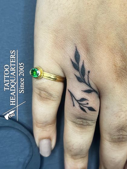A delicate tattoo of leafy branches on the finger, designed to complement the client's ring.