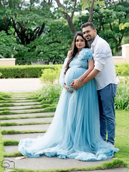 A full-length portrait of the couple in the park, showcasing the magnificent blue gown against the natural greenery.