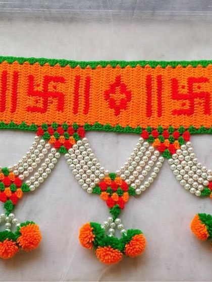 This toran features auspicious Swastik symbols in a vibrant orange, green, and red color palette, perfect for festive occasions.