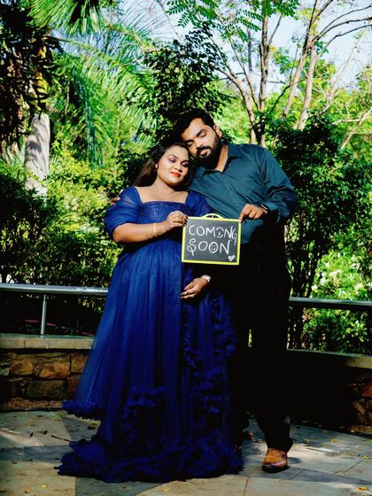 An intimate outdoor portrait of a couple holding a "Coming Soon" sign. The soft lighting and their close embrace make this a sweet and heartfelt announcement.