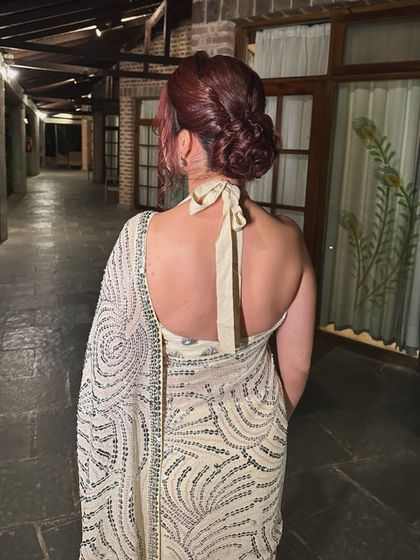 A soft, twisted knot updo for a chic saree look. The hairstyle is designed to complement the halter neck, creating a very elegant and polished silhouette.