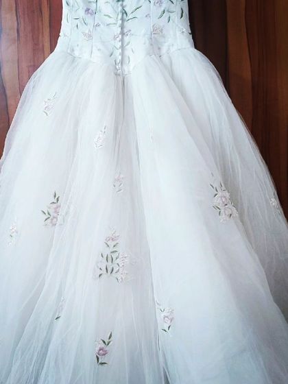 A full view of the embroidered white gown, showing the button details on the back of the bodice and the scattered floral embroidery on the skirt.