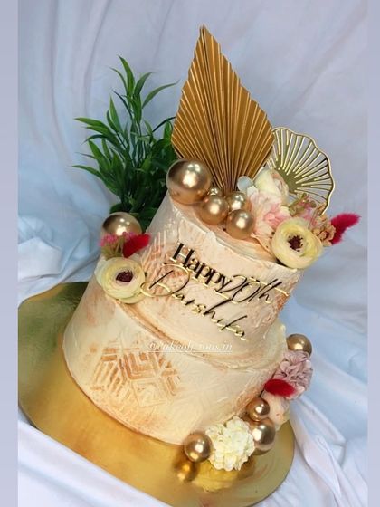 A classic two-tier cake in white and gold, elevated with intricate stenciling and modern gold toppers. This design is perfect for an elegant 20th birthday or an intimate engagement party.