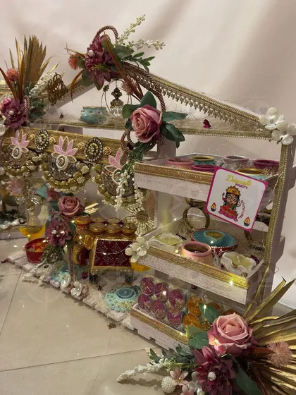 A custom Diwali hamper featuring a multi-tiered stand decorated with 'gota patti' work and roses. It's filled with small, hand-painted 'diyas' and other festive trinkets.