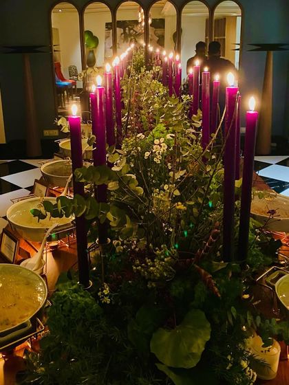 A beautifully arranged buffet table for an intimate soirée, with tall purple candles and lush greenery creating a dramatic and elegant look.