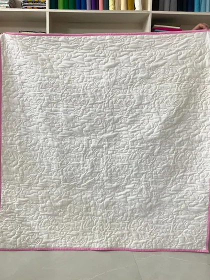 The solid white back of the quilt, which highlights the dense, loopy quilting pattern.