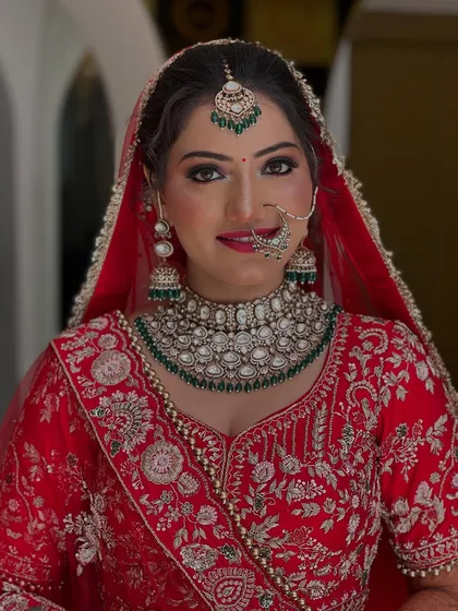 A full-face portrait of our bride in red. The makeup is perfectly balanced, with defined eyes and a neutral lip color to let the stunning green jewelry stand out.