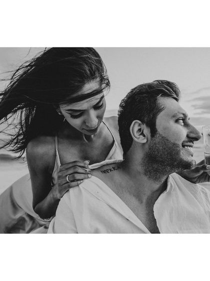 A candid black and white photo of the couple enjoying a glass of champagne on the beach, full of life and laughter.