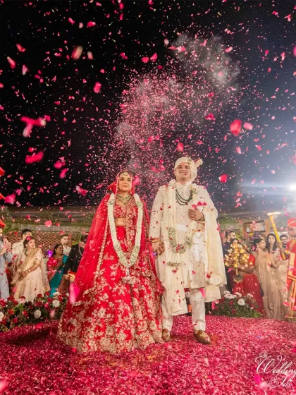 A classic wedding moment, elevated. The couple stands united as guests shower them in a sea of red rose petals, creating a vibrant and joyous photograph we helped orchestrate.