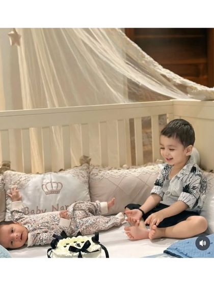 Another angle of this sweet sibling moment. The newborn is lying next to a personalized "Baby Nar" pillow, a cherished part of their new nursery.