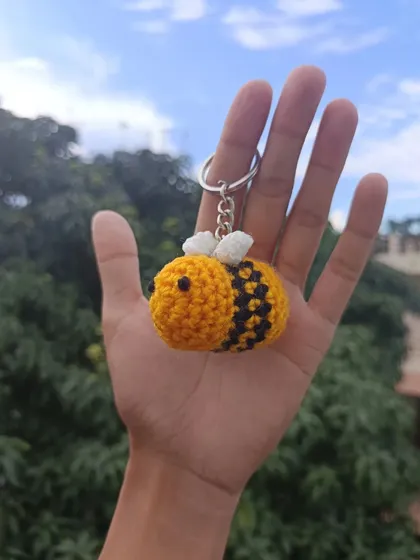 A single bee keychain held in my hand, showcasing its cute, rounded shape and detailed stripes.