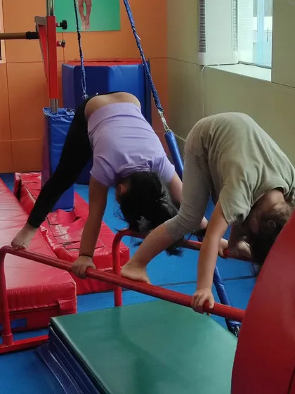 Two children use the bars to assist with a forward fold stretch, a creative way to improve flexibility and hamstring mobility.