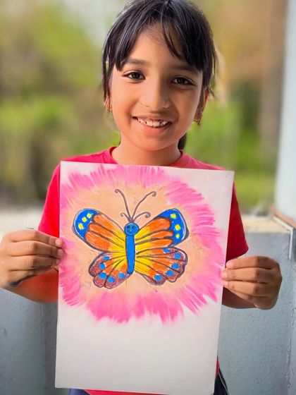 A student holds up her beautifully colored butterfly, showcasing her skill with blending and creating a glowing effect with pastels.