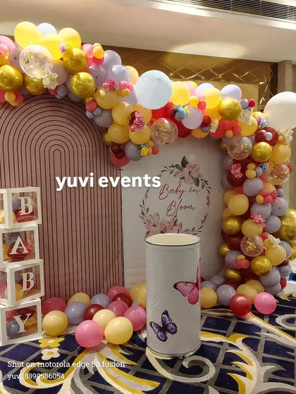 A "Baby in Bloom" themed baby shower backdrop with a colorful balloon arch and transparent "BABY" blocks.