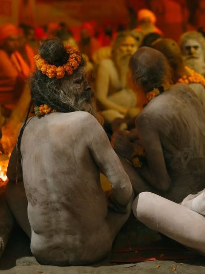Naga sadhus sit together around a fire, their bodies covered in ash. The scene has a timeless, almost prehistoric feel, capturing a moment of ancient brotherhood.