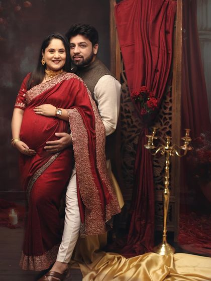 Saree serenity. This lovely couple portrait in matching red tones captures the elegance of maternity, with the rich fabric of the saree beautifully draping over the baby bump.