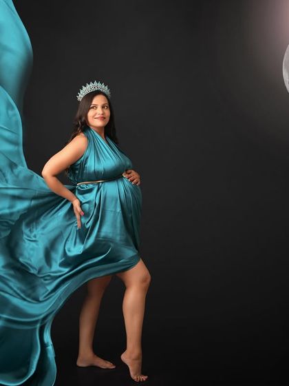 A creative portrait combining a flowing teal gown with a full moon. The mom-to-be, wearing a crown, looks like a celestial goddess in this magical composition.