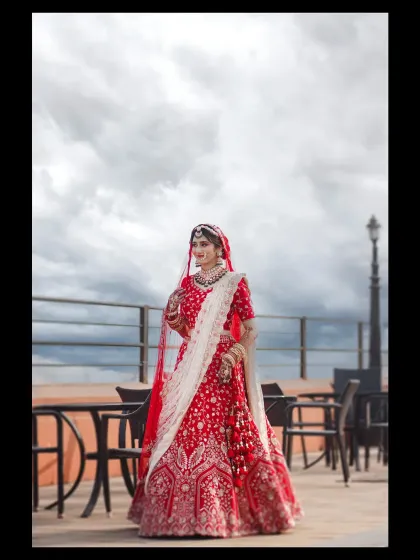 A stunning full-length bridal portrait against a cloudy sky. The bride in her traditional red lehenga looks absolutely majestic.