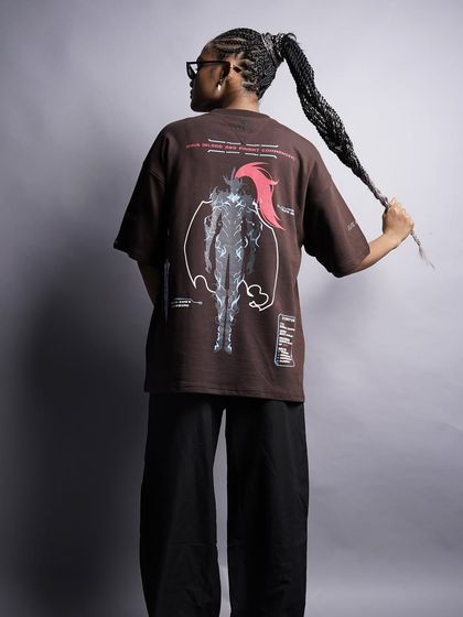 A full back view of the brown graphic tee, allowing the detailed anime-inspired artwork to be the hero of the shot. The model's pose adds a playful touch.